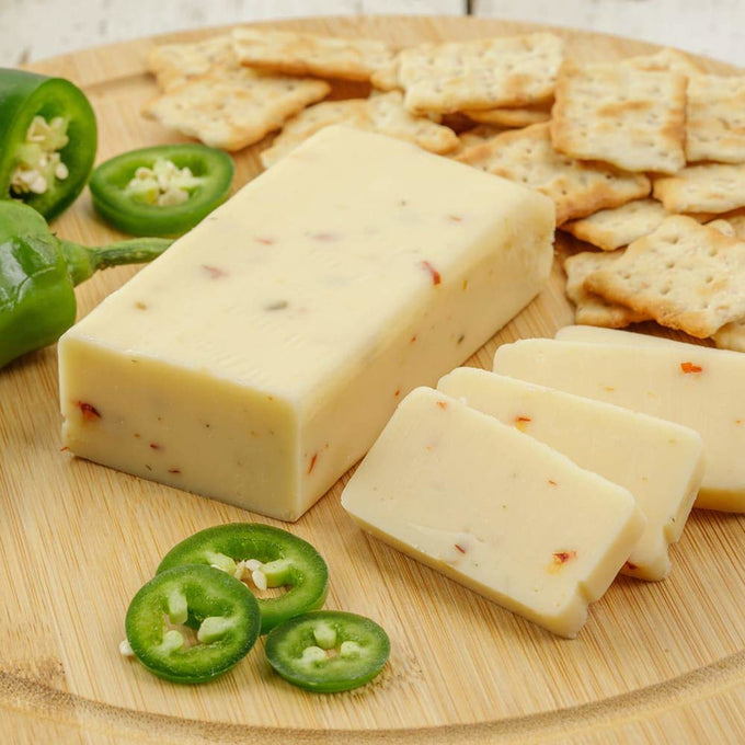 Handcrafted shelf-stable cheese block infused with spicy pepper flakes, sliced and served on a wooden board with crackers and fresh jalapeño slices, ideal for Kitchen & Food, Snacks and Sweets, Pantry, USA Made, Best Sellers, and Promo Eligible collections.