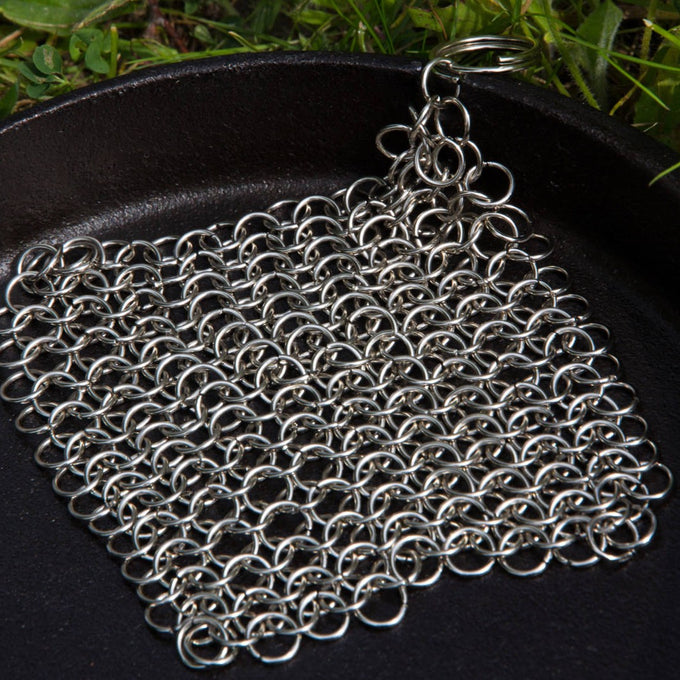 Handcrafted stainless steel chainmail scrubber with keyring handle resting on a cast iron skillet, designed for heavy-duty cleaning, featured in Home & Decor and Household Cleaning collections.