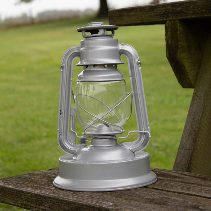 Handcrafted silver metal Rayo Royal Lantern with clear glass globe and protective wire frame, designed for durable bright lighting in farm, garden, camping, and emergency use.