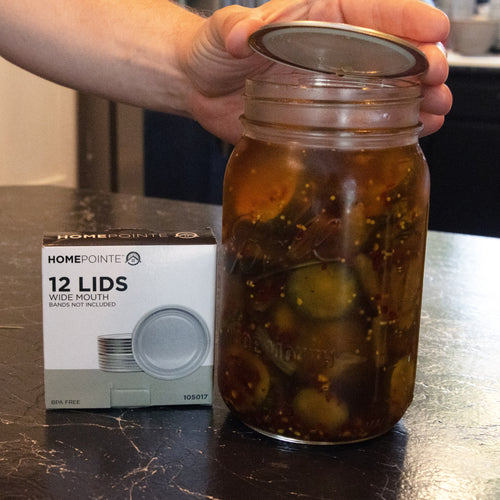 Hand holding a wide-mouth canning lid above a glass jar filled with pickles, next to a box of 12 BPA-free lids, perfect for Kitchen & Food, Food Preservation, Canning, and Best Sellers collections.