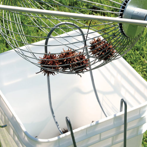 Metal wire nut gatherer with wooden handle holding sweet gum seed pods above a white collection bucket, designed for effortless yard cleanup; featured in Farm, Garden & Tool, Lawncare, Best Sellers, and Promo Eligible collections.