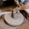 Close-up of hands shaping clay on a potter's wheel in a rustic workshop, showcasing the handmade craftsmanship behind USA made stoneware for Kitchen & Food and Dinnerware collections.