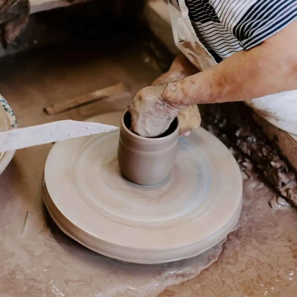 Close-up of hands shaping clay on a potter's wheel in a rustic workshop, showcasing the handmade craftsmanship behind USA made stoneware for Kitchen & Food and Dinnerware collections.