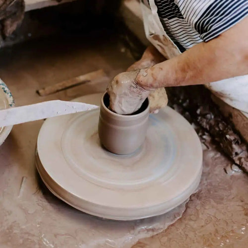 Close-up of hands shaping clay on a potter's wheel in a rustic workshop, showcasing the handmade craftsmanship behind USA made stoneware for Kitchen & Food and Dinnerware collections.