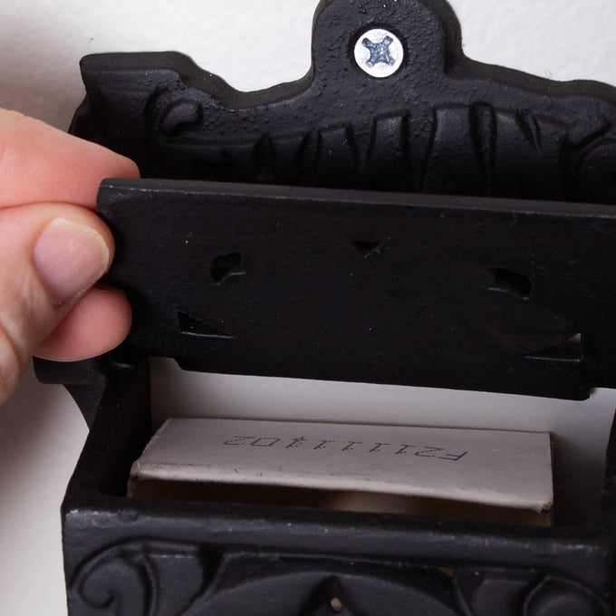 Handcrafted black cast iron wall-mounted matchbox holder with vintage decorative details and a hinged lid, made in USA, perfect for Home & Decor and Household Helpers collections.