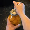Hands labeling a glass jar filled with preserved fruit using a silver metal canning lid with a BPA-free sealing compound, set on a dark countertop, Kitchen & Food collection.