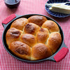 Freshly baked golden brown dinner rolls in a seasoned cast iron skillet with red silicone handles, shown with butter on a blue dish, featured in Kitchen & Food, Cookware, Cast Iron, USA Made, Best Sellers, and Promo Eligible collections.