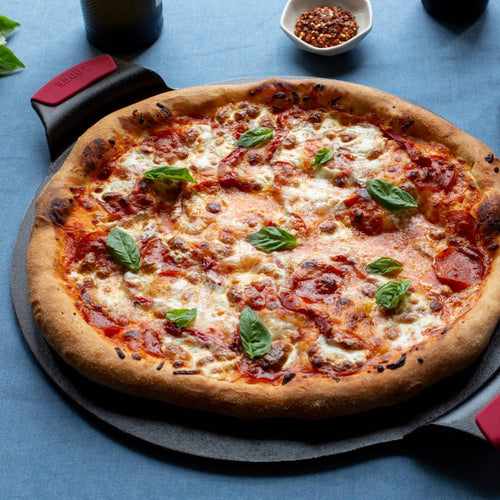 Handcrafted 15 inch cast iron pizza pan with dual handles and red silicone grips holding a pepperoni pizza topped with melted cheese and fresh basil, featured in Kitchen & Food, Cookware, Cast Iron, USA Made, Best Sellers, Promo Eligible collections.