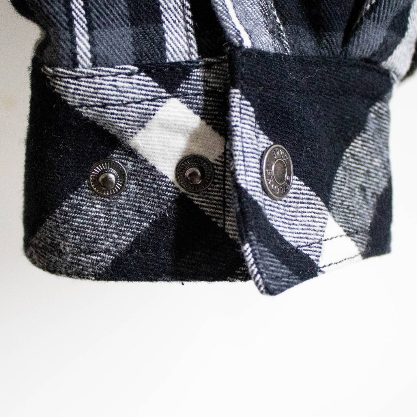 Close-up of a handcrafted black and white plaid flannel cuff featuring detailed woven texture and metal snap buttons, highlighting quality in clothing and health & wellness collections.