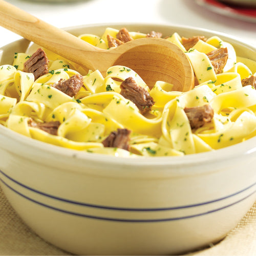 Bowl of wide egg noodles mixed with tender chunks of handcrafted canned beef, lightly garnished with fresh herbs and served with a wooden spoon for Farm, Garden & Tool, Kitchen & Food, Emergency Supplies, Food, Meats, Best Sellers, and Promo Eligible collections.