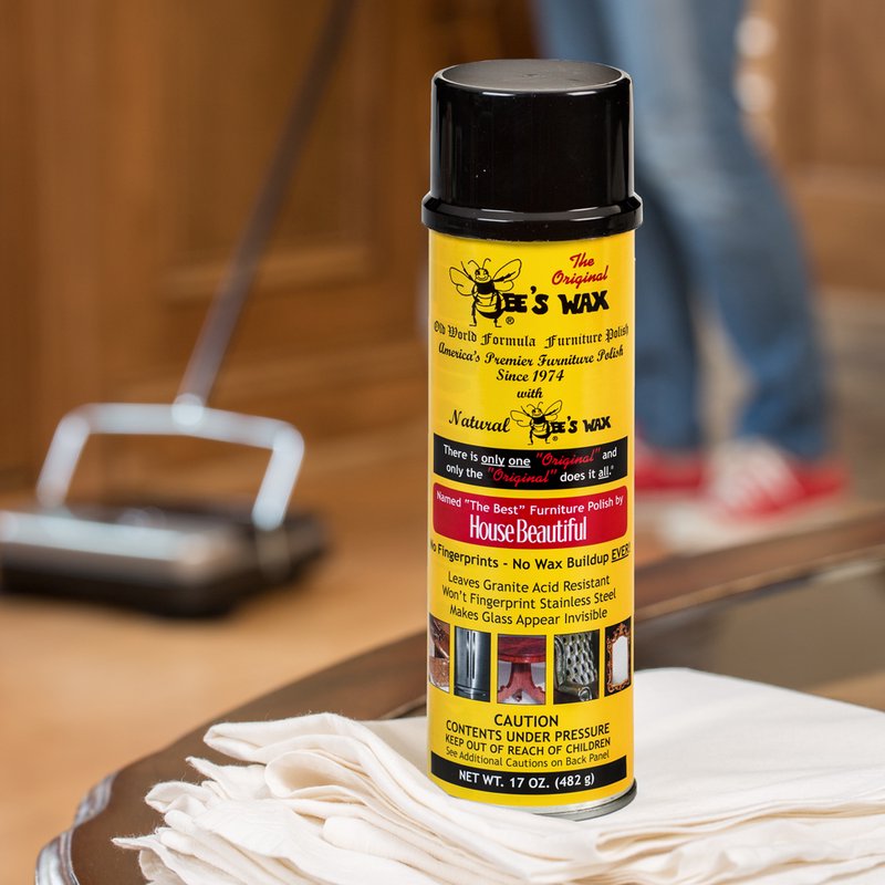 Yellow can of beeswax polish with a black cap, featuring text about no wax buildup, fingerprint resistance, and granite protection, displayed on a white cloth in a home cleaning environment, associated with Home & Decor, Household Cleaning, Cleaners and Polishes, USA Made, Best Sellers, and Promo Eligible collections.
