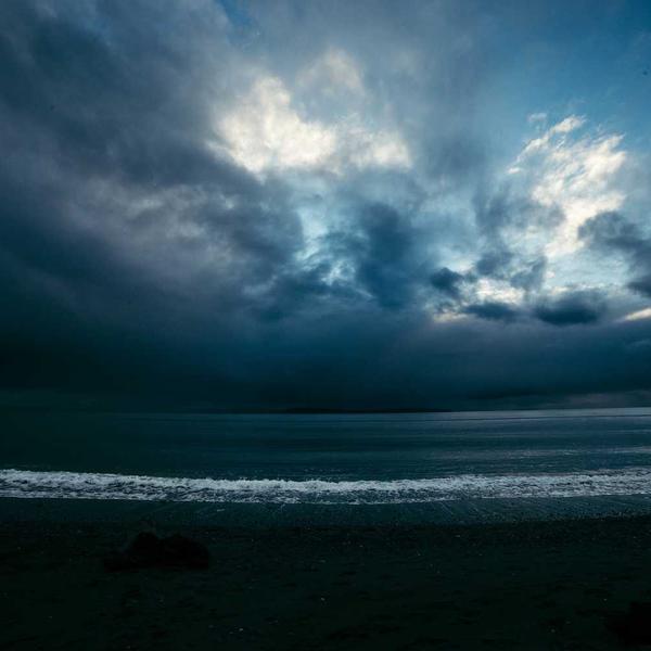 Dark moody seascape with stormy clouds overhead, waves gently breaking on the shore, evoking a calm yet dramatic coastal atmosphere for Best Sellers and P3 Testing collections.