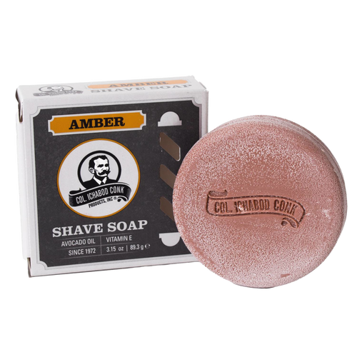 Round amber-colored shaving soap bar with embossed branding beside its box, containing avocado oil and vitamin E, crafted in USA, featured in Health & Wellness and Grooming collections.