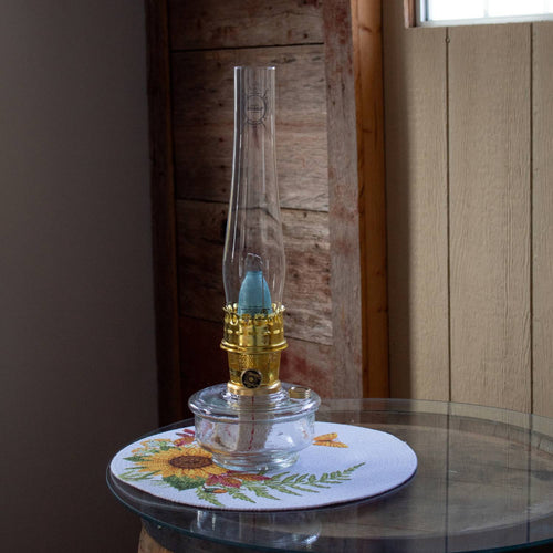Handcrafted clear Regency-style oil lamp with polished brass burner and tall glass chimney, displayed on a glass table with a floral placemat, ideal for Farm, Garden & Tool and Emergency Supplies collections.