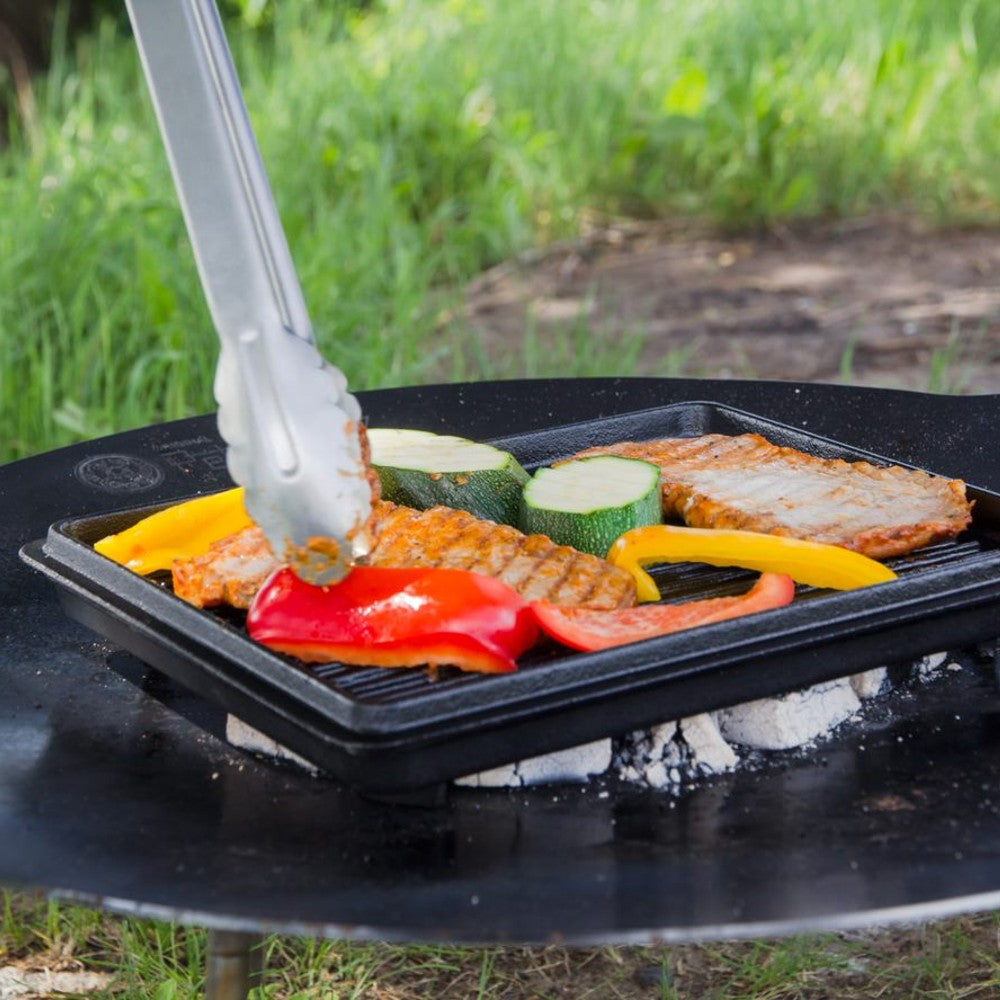 Square cast iron grill pan cooking seasoned pork chops and colorful bell peppers over glowing charcoal outdoors, ideal for farm, garden, camping, kitchen, cookware, and cast iron collections.