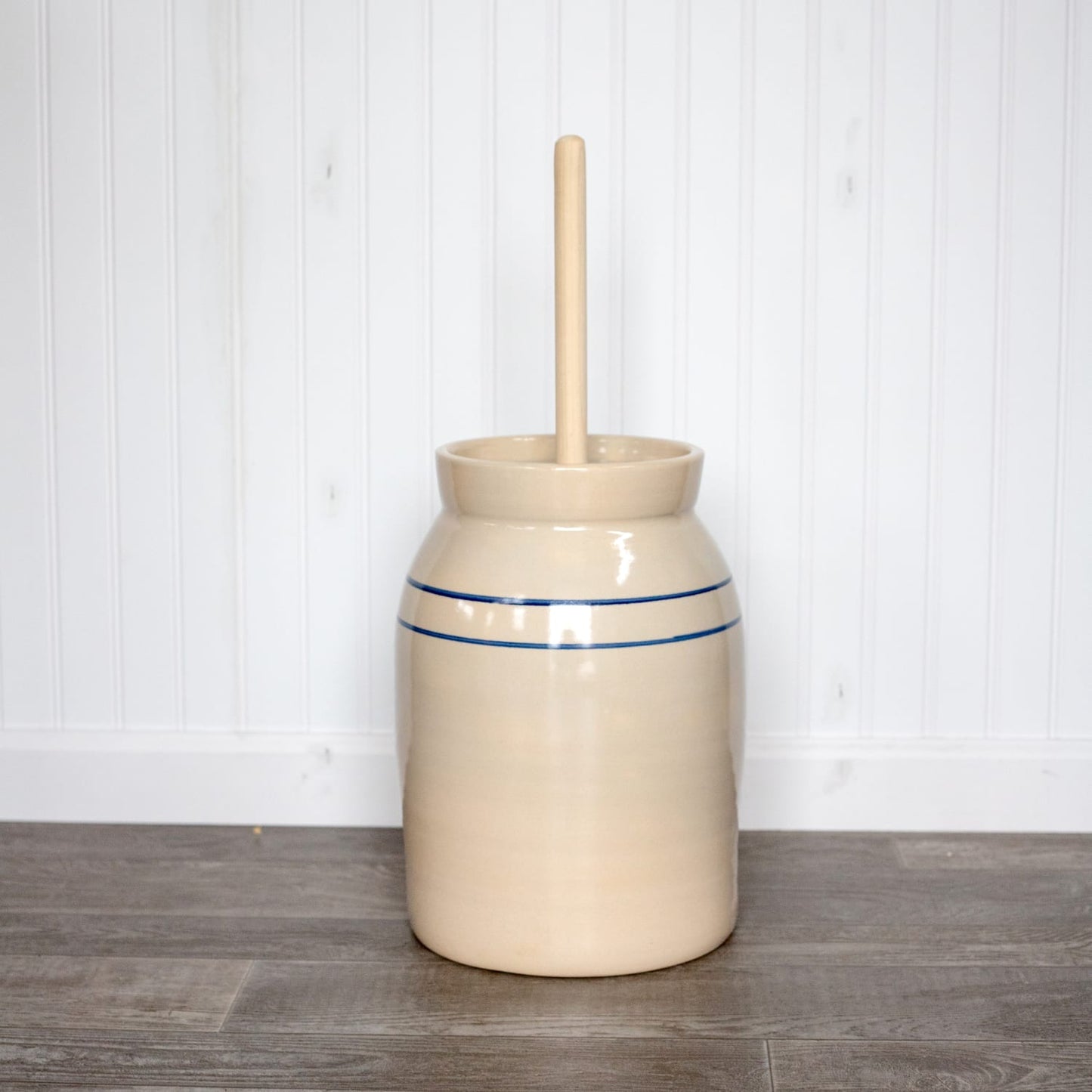 Handcrafted stoneware butter churn in natural stone color with smooth unfinished wooden dasher and classic double blue stripe, made in USA, ideal for Kitchen & Food and Specialty Equipment collections.