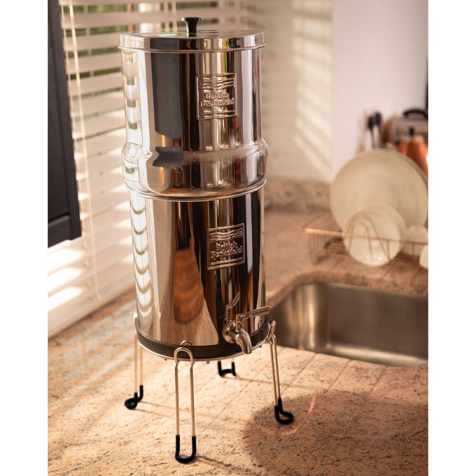 Polished stainless steel gravity water filter set elevated on a handcrafted sturdy stand with protective feet, designed for convenient dispensing in Appliances, Emergency Supplies, and Water Heating and Treatment collections.