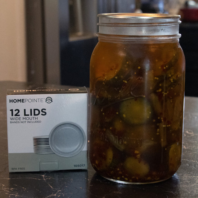 Glass jar of homemade pickles sealed with a wide-mouth lid next to a box of 12 BPA-free sealing compound lids, ideal for Kitchen & Food, Food Preservation, Canning, and Best Sellers collections.