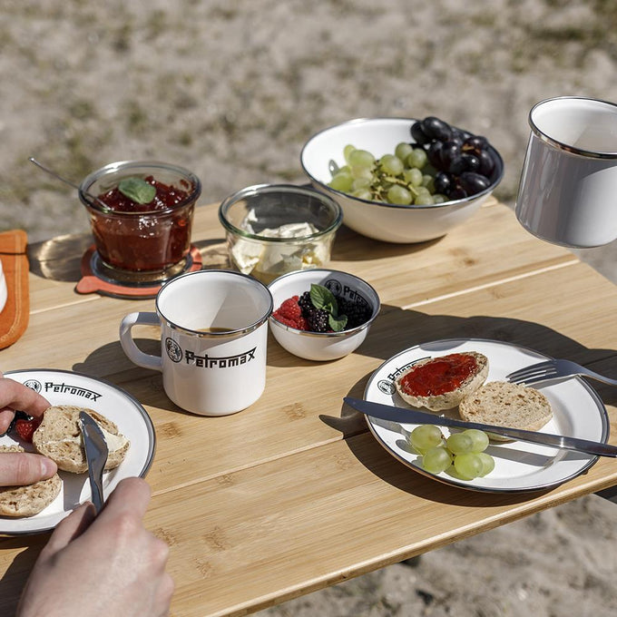 White enamel bowls, plates, and mugs with black rims and logos, featuring fresh fruit and breakfast items on a wooden outdoor table, perfect for Farm, Garden & Tool, Kitchen & Food, Camping, Dinnerware, Best Sellers, and Promo Eligible collections.