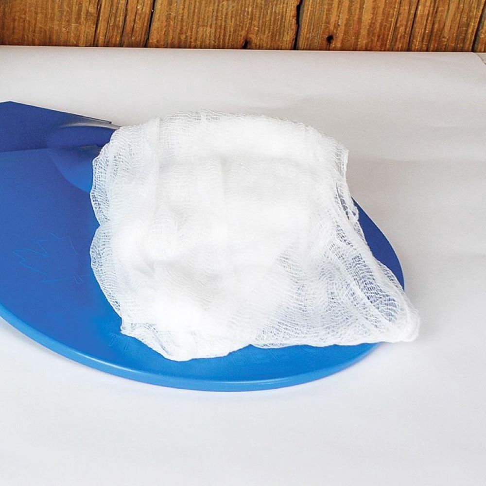 White loosely woven cheesecloth draped over a blue plastic cutting board on a light tabletop, suitable for use in farm, garden, and maple syrup sugaring supplies collections.