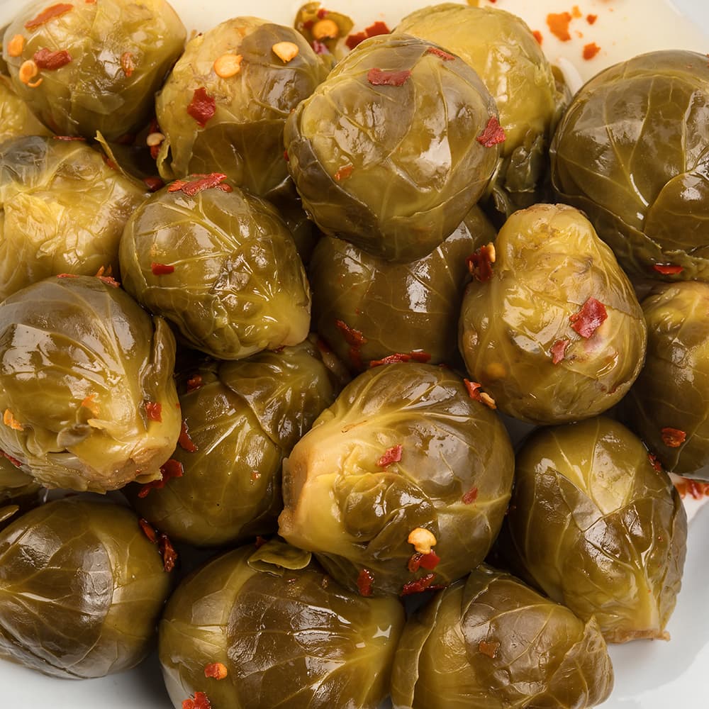 Close-up of handcrafted pickled Brussels sprouts in a tangy, spiced brine with visible red pepper flakes, made in USA and perfect for Kitchen & Food, Pantry, Best Sellers, and Promo Eligible collections.