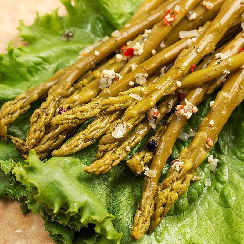 Handcrafted pickled asparagus spears seasoned with cracked pepper and spices, resting on fresh green lettuce, showcasing tangy flavor for Kitchen & Food, Pantry, USA Made, and Best Sellers collections.