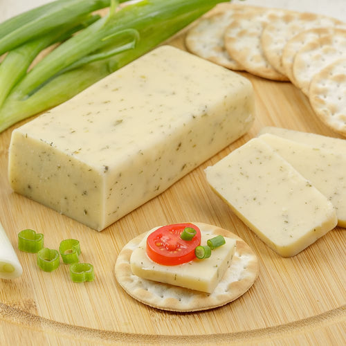 Handcrafted shelf-stable cheese block with herb flecks, sliced and served on round crackers topped with tomato and green onion, perfect for Kitchen & Food, Pantry, USA Made, and Best Sellers collections.
