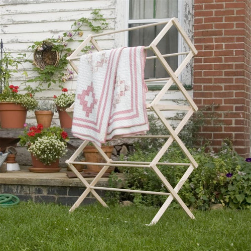 Large handcrafted wooden drying rack with multiple tiers, holding a quilt outdoors against a rustic brick and siding backdrop, Amish made in USA, ideal for Home & Decor and Laundry Supplies collections.