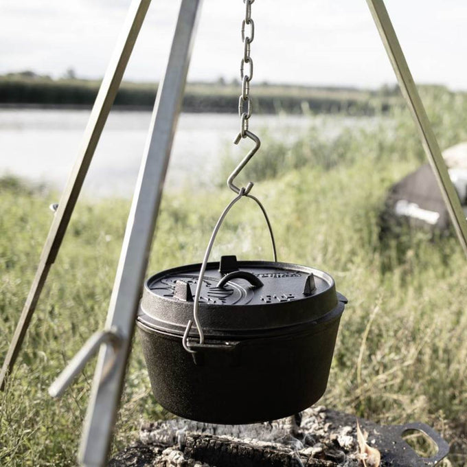 Heavy cast iron Dutch oven with flat base, suspended over an open fire using a metal chain and tripod, ideal for outdoor cooking and featured in Kitchen & Food, Cookware, Cast Iron, Best Sellers, Promo Eligible collections.