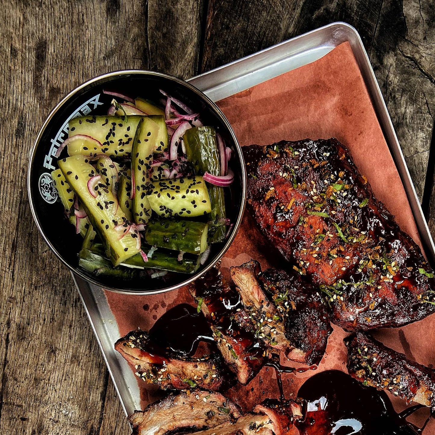 Black enamel bowl filled with pickled cucumbers and red onions, placed on a metal tray with grilled ribs garnished with herbs, featured in Kitchen & Food, Camping, Dinnerware, and Best Sellers collections.