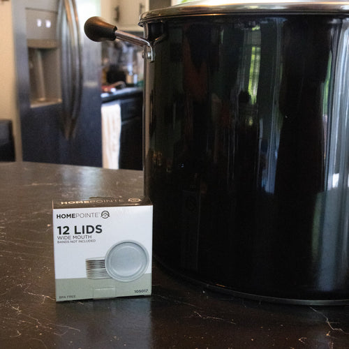 Box of twelve wide-mouth canning lids with BPA-free sealing compound next to a black enamel pot, perfect for Kitchen & Food, Food Preservation, Canning, Canning Jar Lids and Bands, Best Sellers, and Promo Eligible collections.