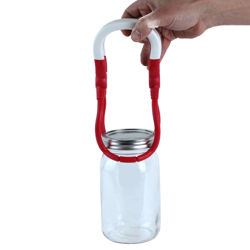 Hand holding a one-handed jar lifter with a red and white rounded handle gripping a glass canning jar, designed for safe lifting in kitchen, canning, and food preservation tasks.