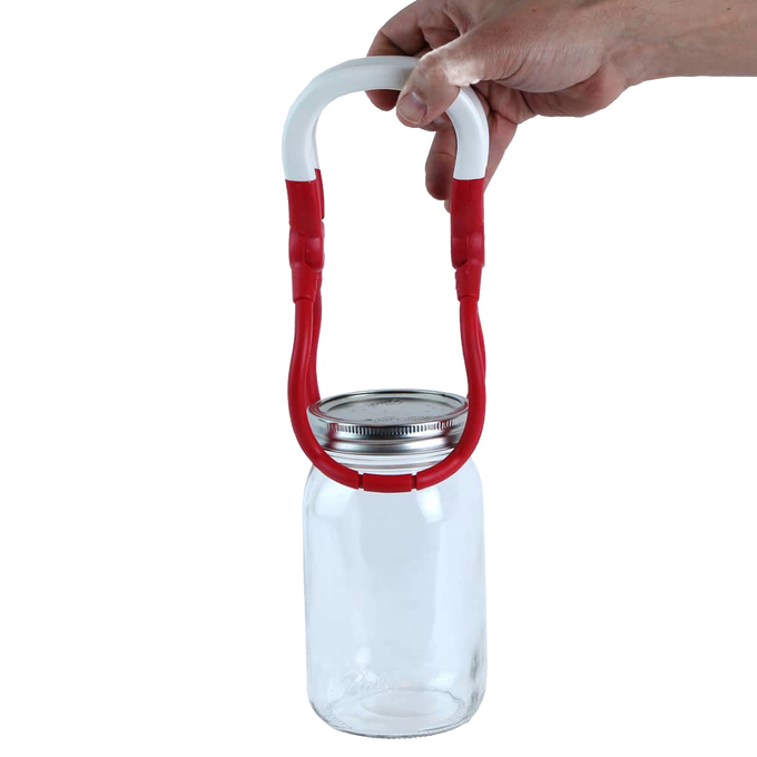 Hand holding a one-handed jar lifter with a red and white rounded handle gripping a glass canning jar, designed for safe lifting in kitchen, canning, and food preservation tasks.
