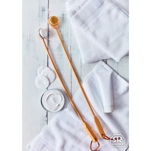 Two long wooden-handled grooming brushes with natural bristles and replaceable pads placed on white towels alongside cotton rounds and a cream tube, styled for Health & Wellness and Grooming and Personal Hygiene collections.
