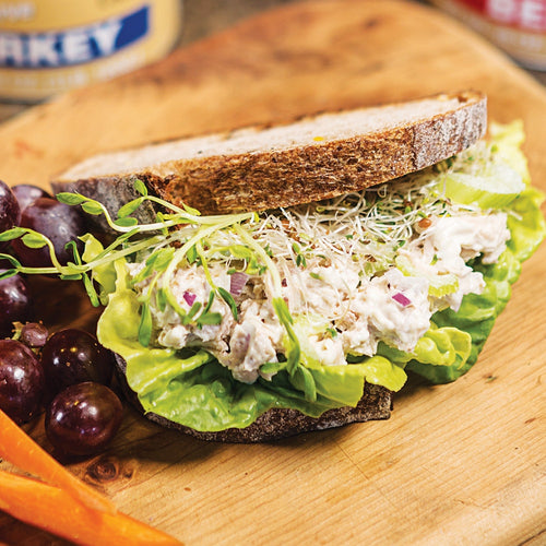 Hearty sandwich with creamy chicken salad, fresh lettuce, sprouts, and diced onions on rustic whole grain bread, served with grapes and carrots, ideal for Kitchen & Food, Food, Meats, Best Sellers, Promo Eligible collections.