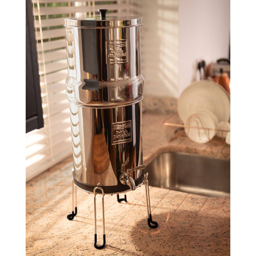 Stainless steel gravity water filter system elevated on a sleek stand with rubber-tipped legs, designed for easy dispensing and kitchen counter convenience, featured in Appliances and Emergency Supplies collections.