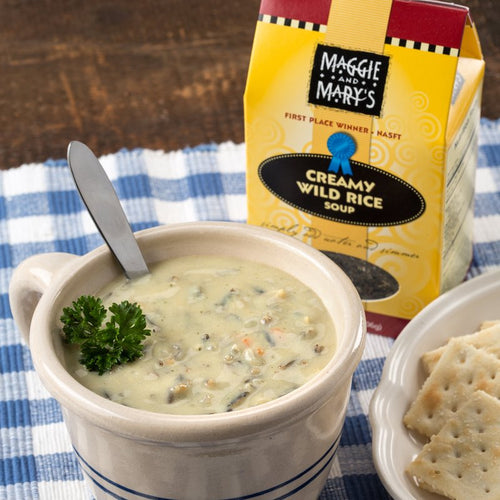 Creamy wild rice soup served in a ceramic bowl with fresh parsley garnish and spoon, accompanied by crackers and Maggie and Mary's handcrafted soup mix packaging, ideal for Kitchen & Food, Dry Goods and Mixes, Soups, USA Made, Best Sellers, and Promo Eligible collections.