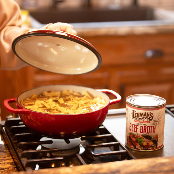 Person lifting lid of red pot with soup or stew made from broth with noodles, next to can of Lehman’s handcrafted beef broth on stovetop in rustic kitchen, featured for Farm, Garden & Tool, Kitchen & Food, Emergency Supplies, Food, Meats, Best Sellers, and Promo Eligible collections.