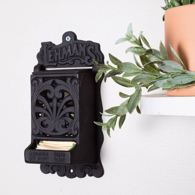 Handcrafted black cast iron wall-mounted matchbox holder with decorative vintage cutout design and Lehman's embossed branding, Amish made in USA, featured in Home & Decor, Household Helpers, and Best Sellers collections.