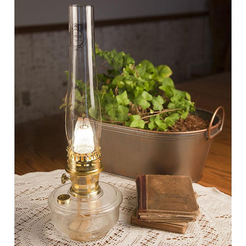 Handcrafted Aladdin Genie III Oil Lamp with clear dimpled glass bowl and polished brass burner, displayed on lace tablecloth beside vintage books and a metal planter, ideal for Farm, Garden & Tool, Lamps & Lighting, and Emergency Supplies collections.