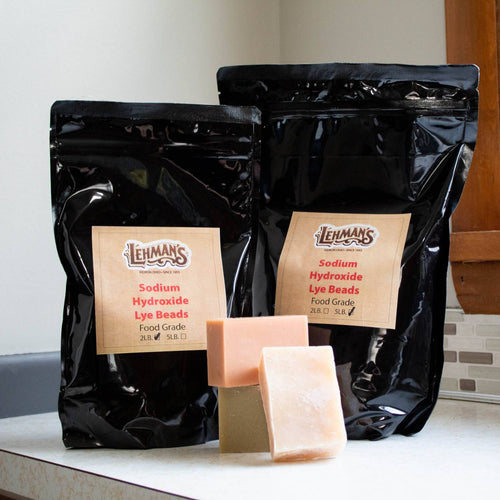 Two resealable black bags of high-grade sodium hydroxide lye beads in 2-lb and 5-lb sizes displayed with three handcrafted soap bars, featured in Health & Wellness, Soaps and Soapmaking, USA Made, and Best Sellers collections.