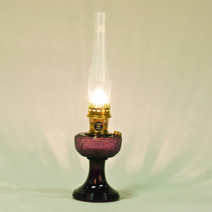 Handcrafted oil lamp with a deep purple Lincoln Drape glass base, tall clear chimney, and polished brass burner glowing softly, perfect for Farm, Garden & Tool, Lamps & Lighting, Oil Lamps, Table Lamps, Best Sellers, Homesteading, and Promo Eligible collections.