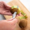 Close-up of a hand using a high carbon stainless steel paring knife with a solid aluminum handle to peel a kiwi fruit on a wooden cutting board, handcrafted and made in USA.