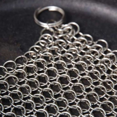Close-up of a handcrafted stainless steel chainmail scrubber with keyring handle resting on a cast iron surface, featured in Home & Decor, Household Cleaning, Cleaning Utensils and Gadgets, Best Sellers, and Promo Eligible collections.