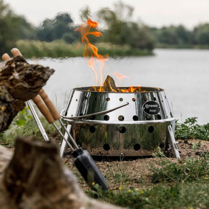 Portable stainless steel Petromax Atago camp grill and fire bowl with perforated sides and fold-out legs, handcrafted for versatile outdoor cooking and cozy fires in Camping and Grilling collections.