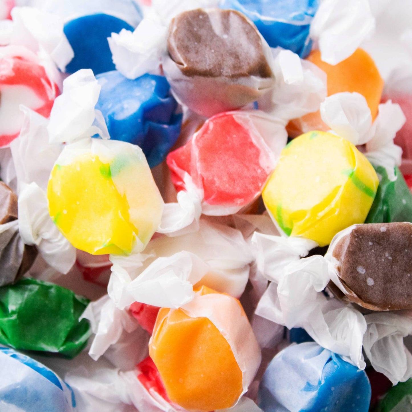 Assorted handmade taffy candies individually wrapped in white wax paper, showcasing vibrant colors and evoking nostalgic flavors from Kitchen & Food, Snacks and Sweets, Best Sellers, and Promo Eligible collections.