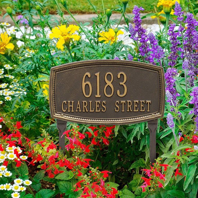 Handcrafted bronze custom address plaque with raised border showing house number and street name, displayed among colorful garden flowers, made in USA, ideal for Home & Decor and Mailboxes and Address Signs collections.