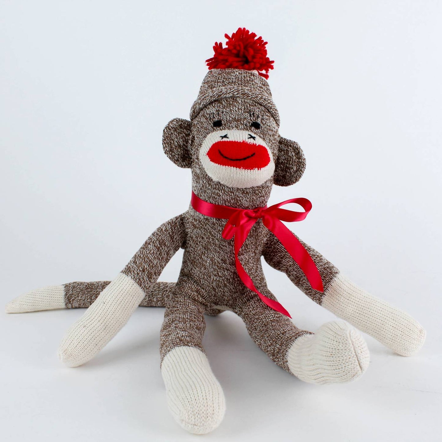 Handcrafted brown and cream sock monkey with a red pom-pom hat and coordinating ribbon bow, made in USA, featured in Toys, Books & Games, USA Made, Children's Toys, Indoor Play, and Best Sellers collections.