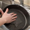 Hand using an extra large handcrafted stainless steel chainmail scrubber to clean a cast iron skillet under running water, part of kitchen cleaning and cookware accessories collections.