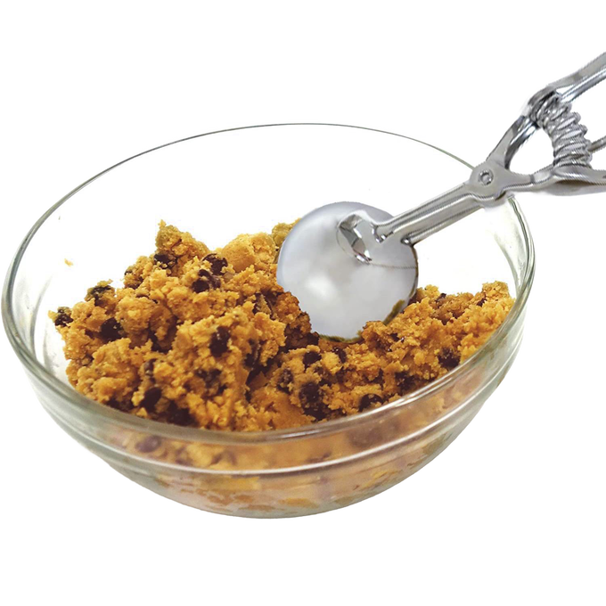 Metal scoop with a spring handle extracting cookie dough from a clear glass bowl, ideal for Kitchen & Food, Bakeware, and Best Sellers collections, handcrafted quality.